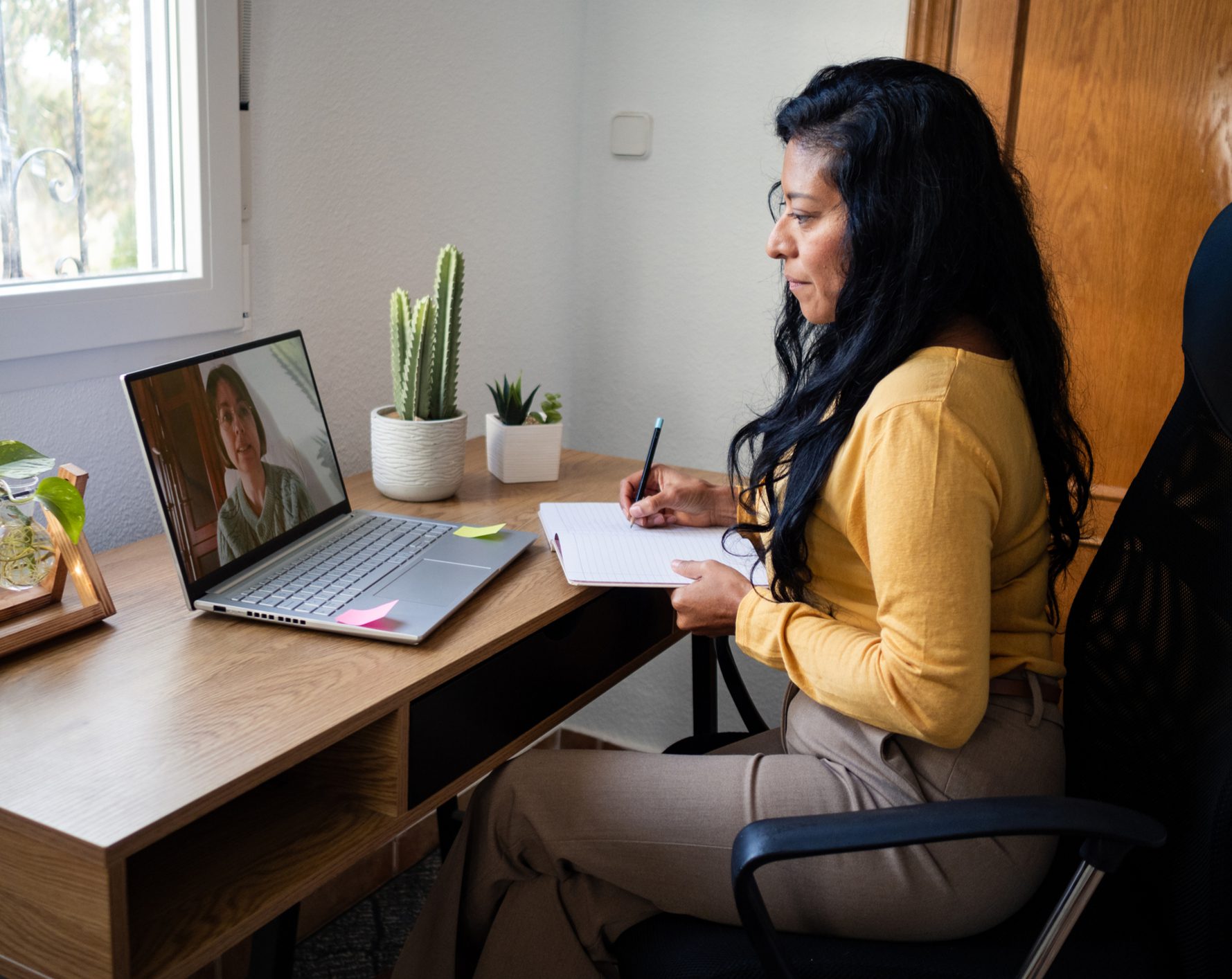 Woman taking notes during video call at desk